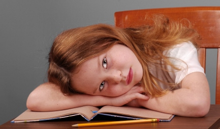 young girl at a desk with her head on her book