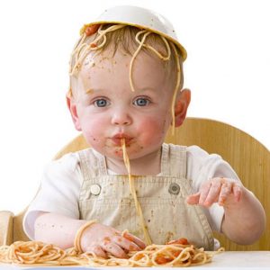 baby eating spaghetti with a bowl on this head