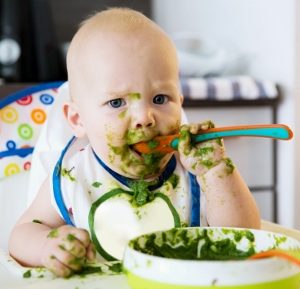 baby eating green food with a spoon